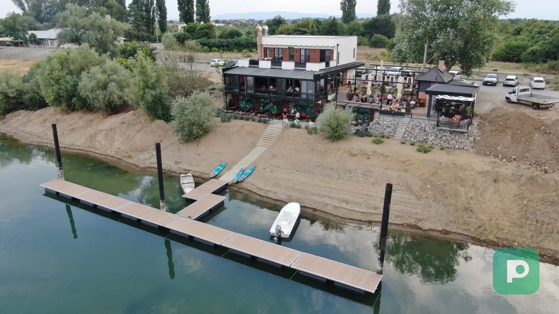 Plastopex pontonski pristan na vodi pored restorana, sa čamcem i prostorom za pristup plovilima.